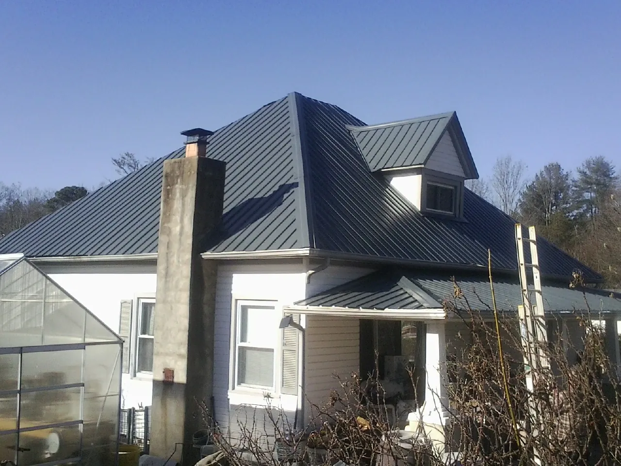 Dark blue standing seam metal roof on a white farmhouse with dormer — Slate & Tile Roof Repair by Roofing Brothers in Kawkawlin