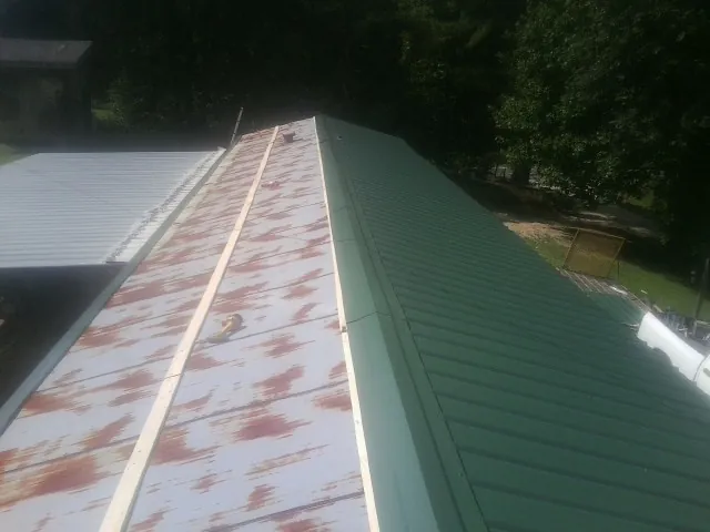 Old rusted panels beside newly installed green metal roofing — Wind Damage Roof Repair by Roofing Brothers in Kawkawlin