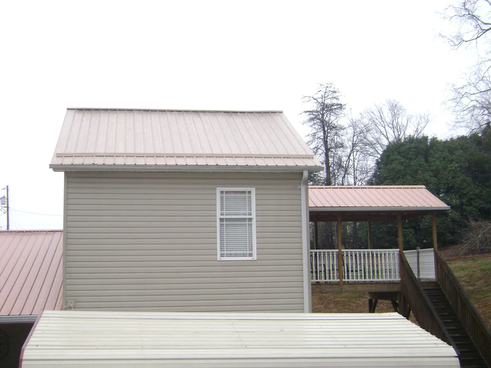 Tan metal roofs on a two story addition and attached porch, from a Roof Replacement job in Kawkawlin